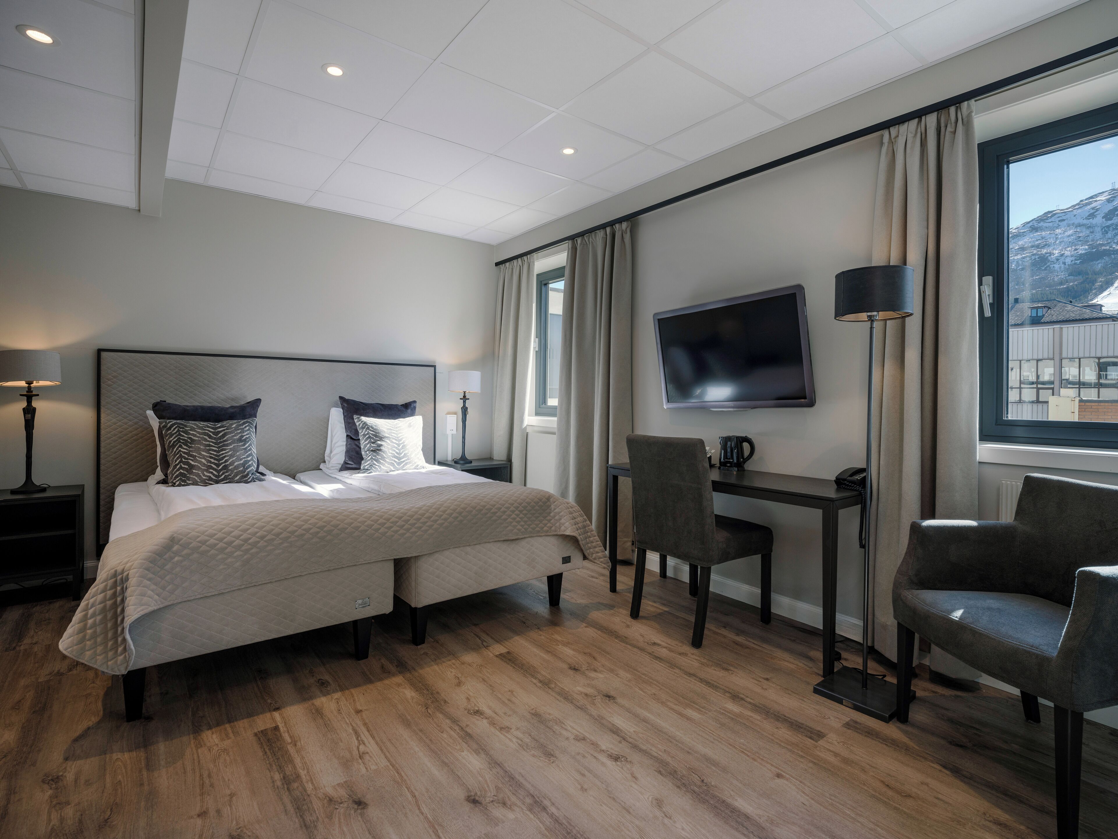 A hotel room with a bed, a desk, a chair, a TV, and a window with a view.