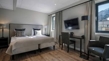 A hotel room with a bed, a desk, a chair, a TV, and a window with a view.