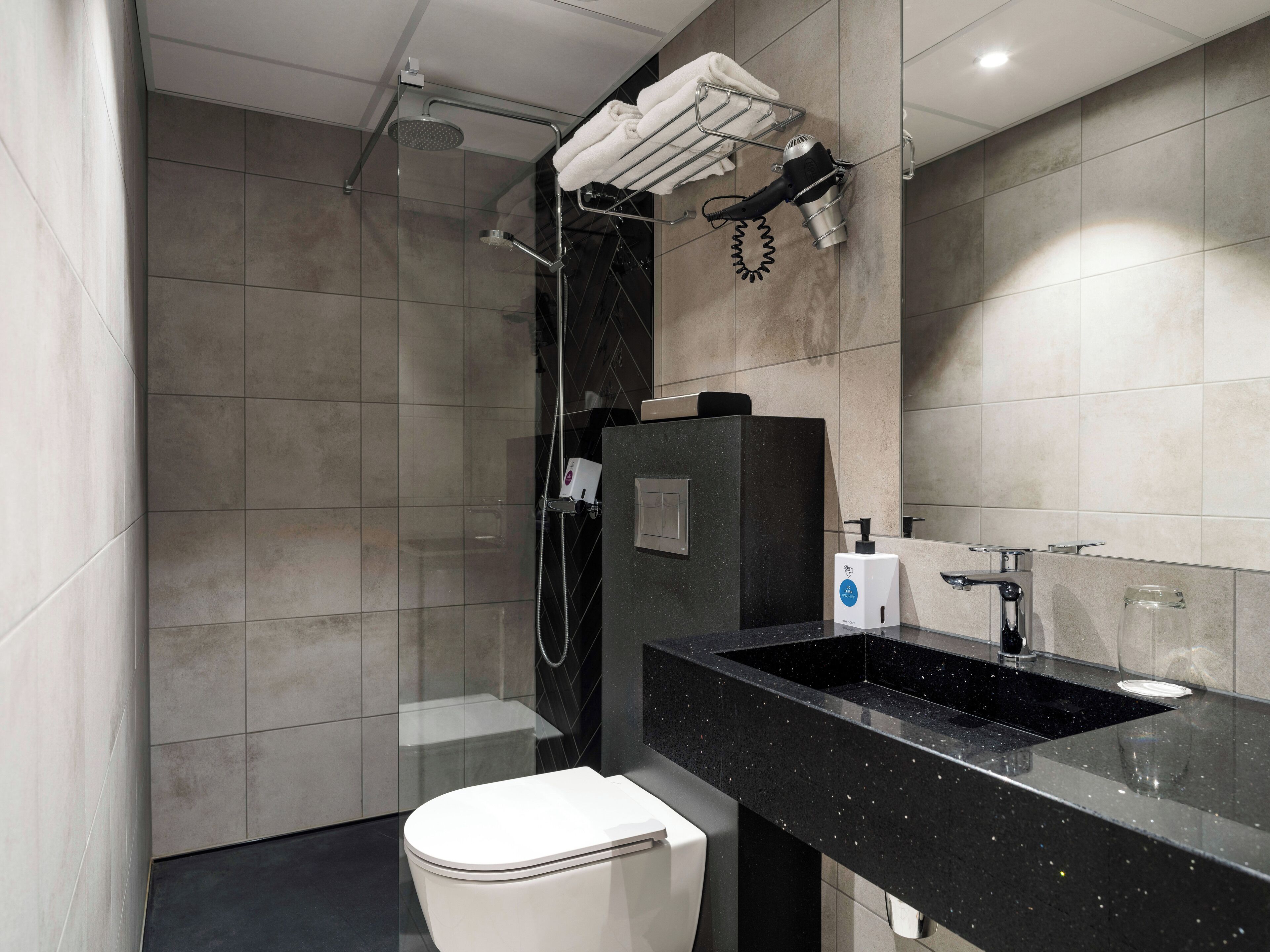 Et moderne badeværelse med en glasafskærmet brusekabine, en sort vask og et hvidt toilet.