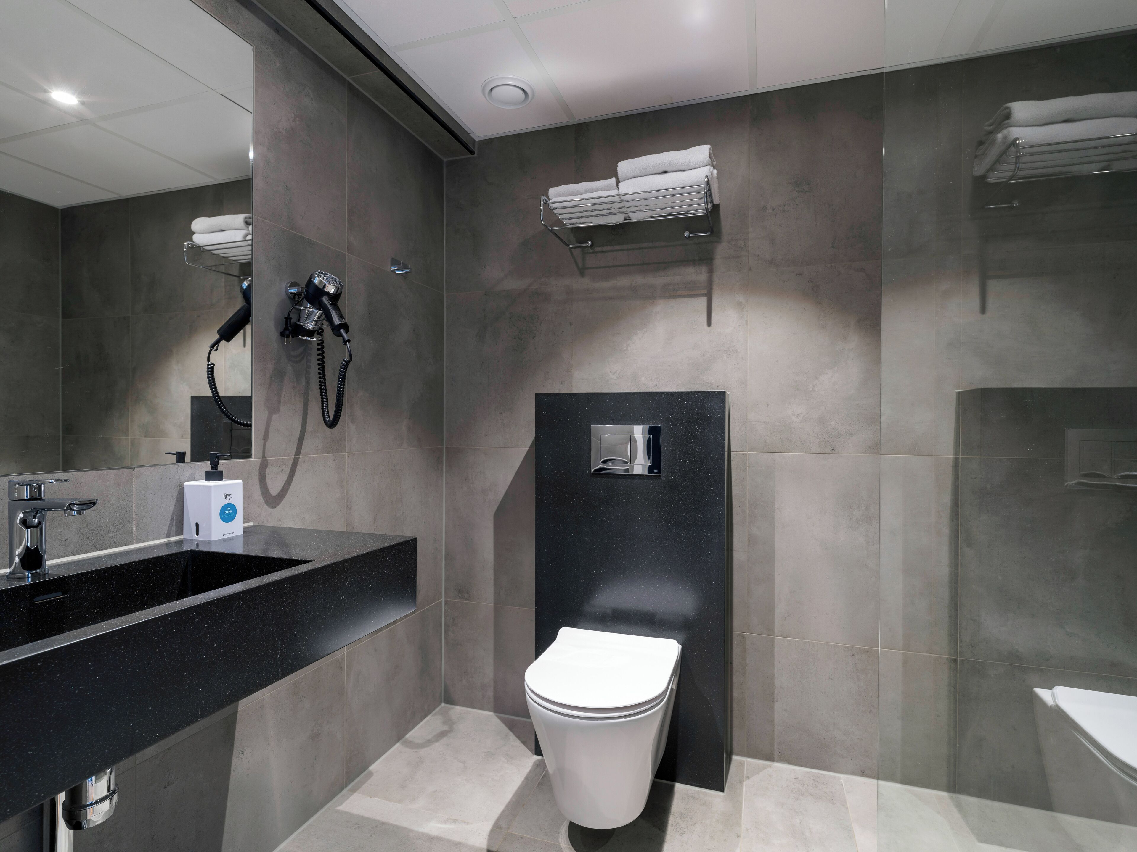 Un baño moderno con un lavamanos negro, un inodoro, una ducha con cabezal de ducha manual y un perchero para toallas.