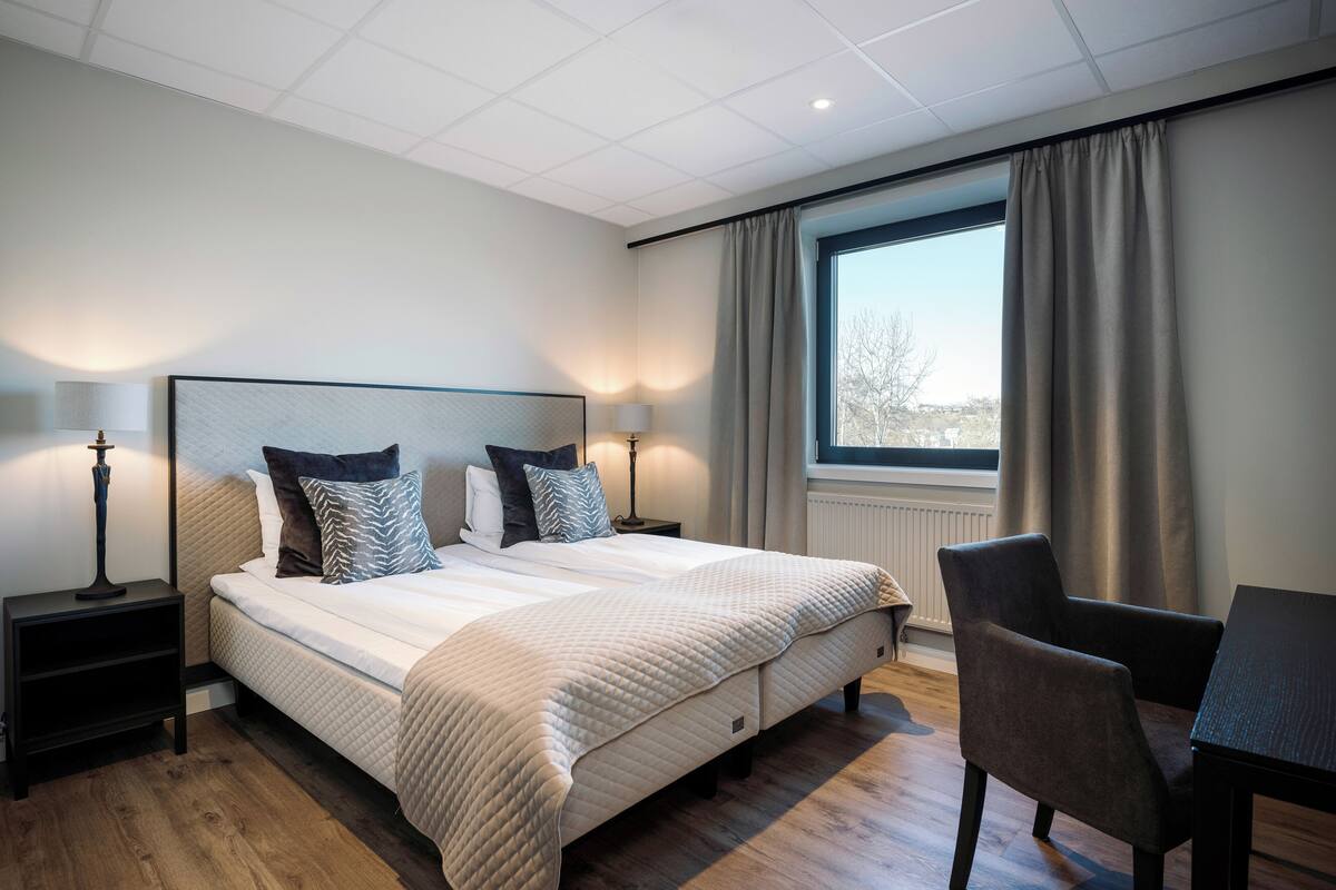 A modern hotel room with a large bed, bedside lamps, a desk, and a view of the outdoors.