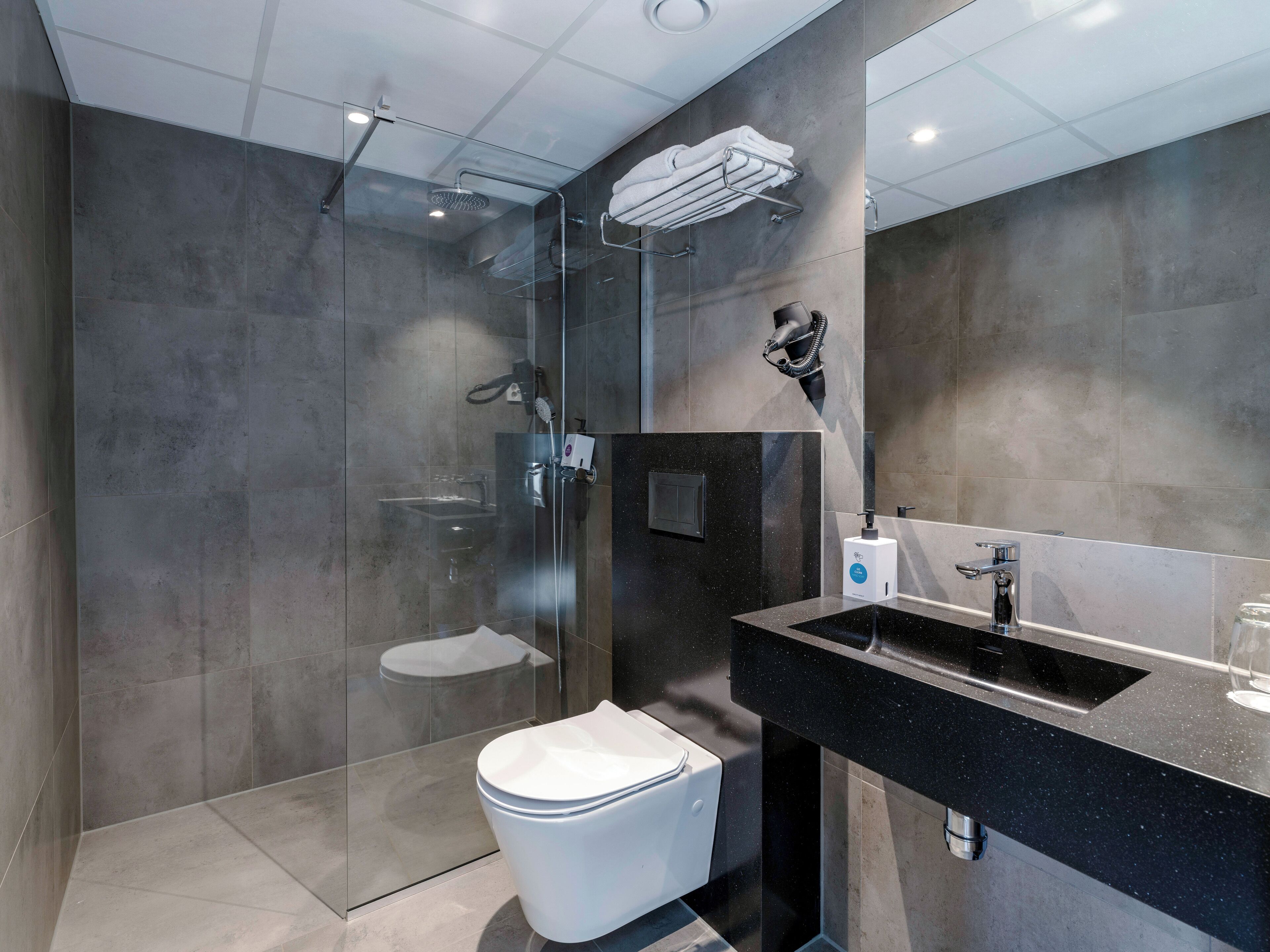 Un baño moderno con ducha de mampara de vidrio, lavamanos negro y retrete blanco.