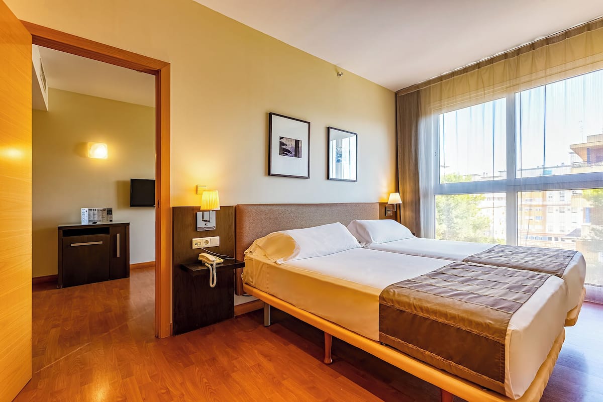 Una habitación de hotel con una cama grande, lámparas de noche, un escritorio con teléfono y una ventana con vistas.