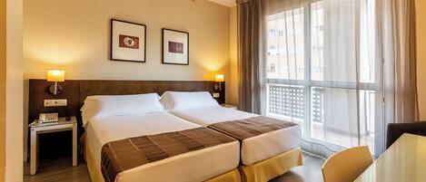 Une chambre d’hôtel avec un lit double, des tables de chevet avec des lampes, une petite table et une vue sur l’extérieur grâce à de grandes fenêtres.