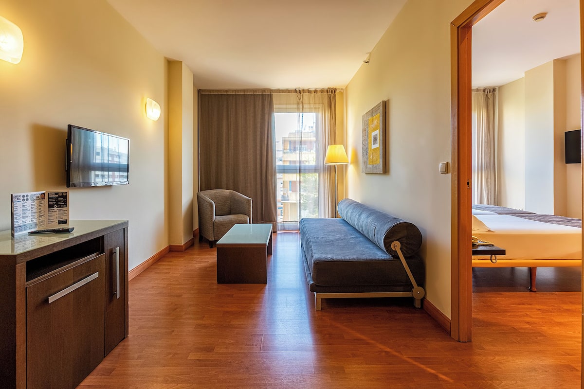 Una habitación de hotel moderna con sofá, televisión, escritorio y cama.