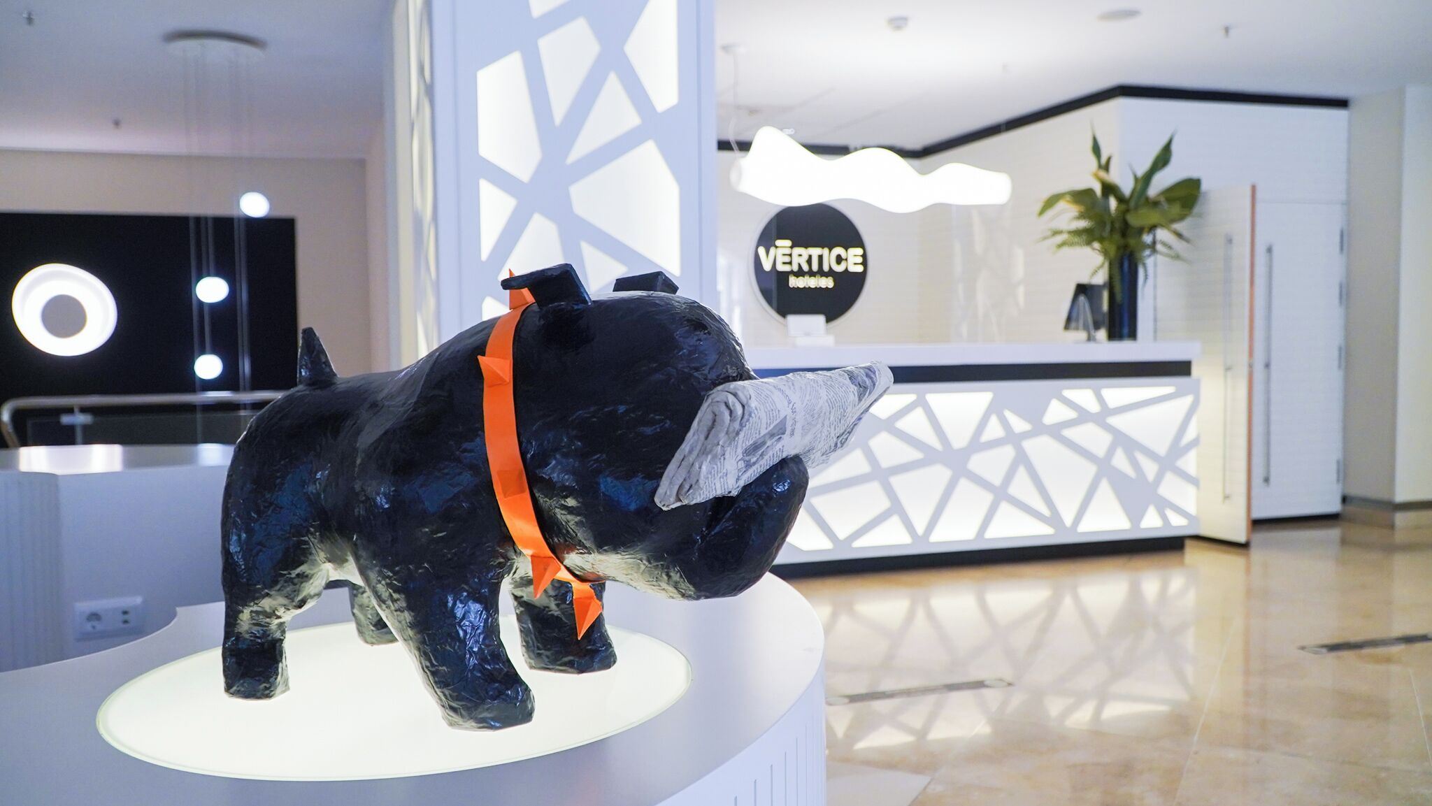 A reception desk with a sign reading "VERTICE Hotels" and a sculpture of a dog wearing a scarf.