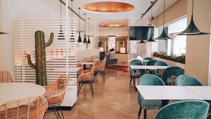 Un espace de restauration moderne avec des chaises en osier, des tables blanches et des luminaires suspendus.