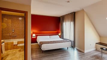 Habitación de hotel con cama, escritorio, baño con ducha y vista al cielo.