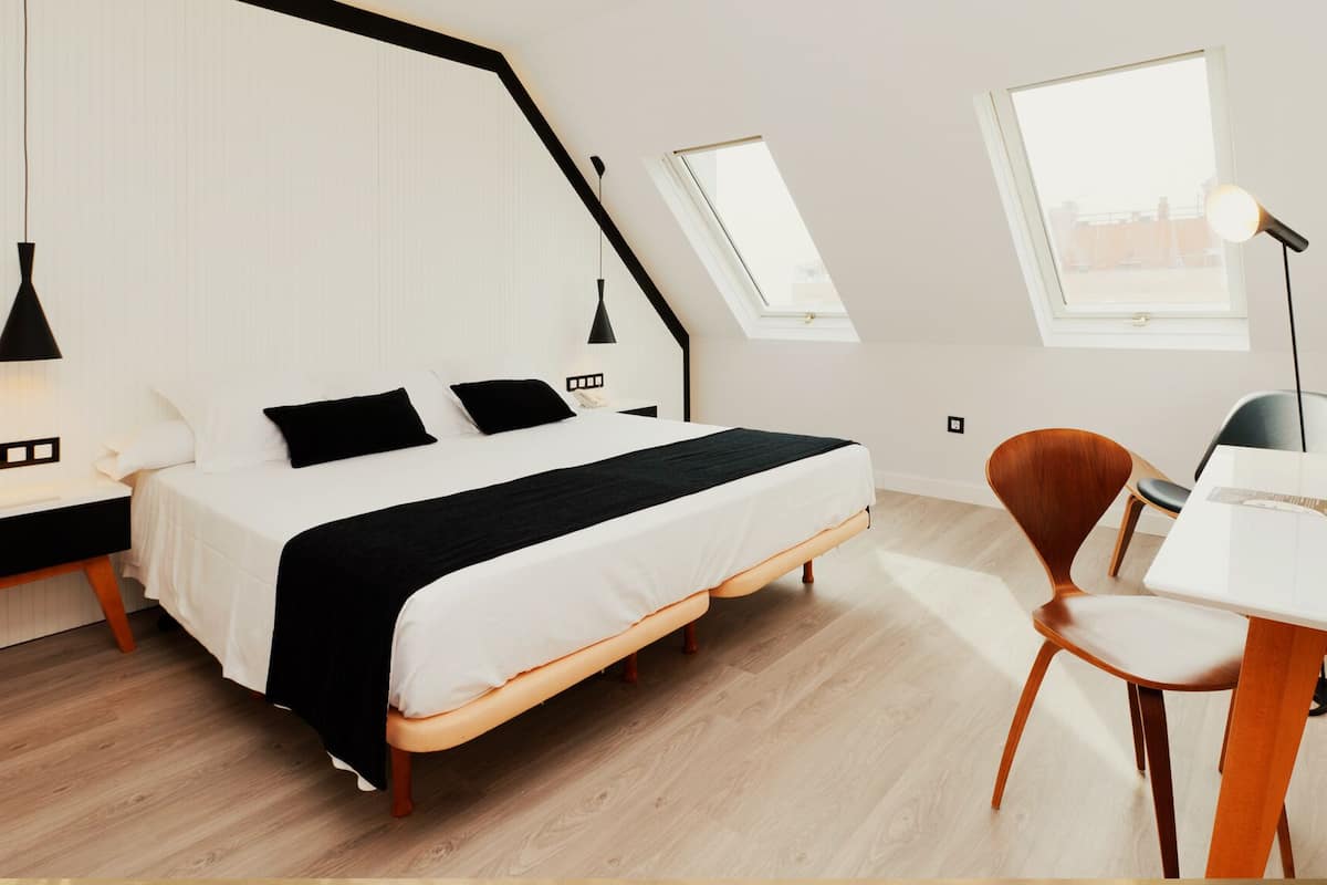 Un dormitorio moderno con cama, mesitas de noche, un escritorio, una silla y dos tragaluces.
