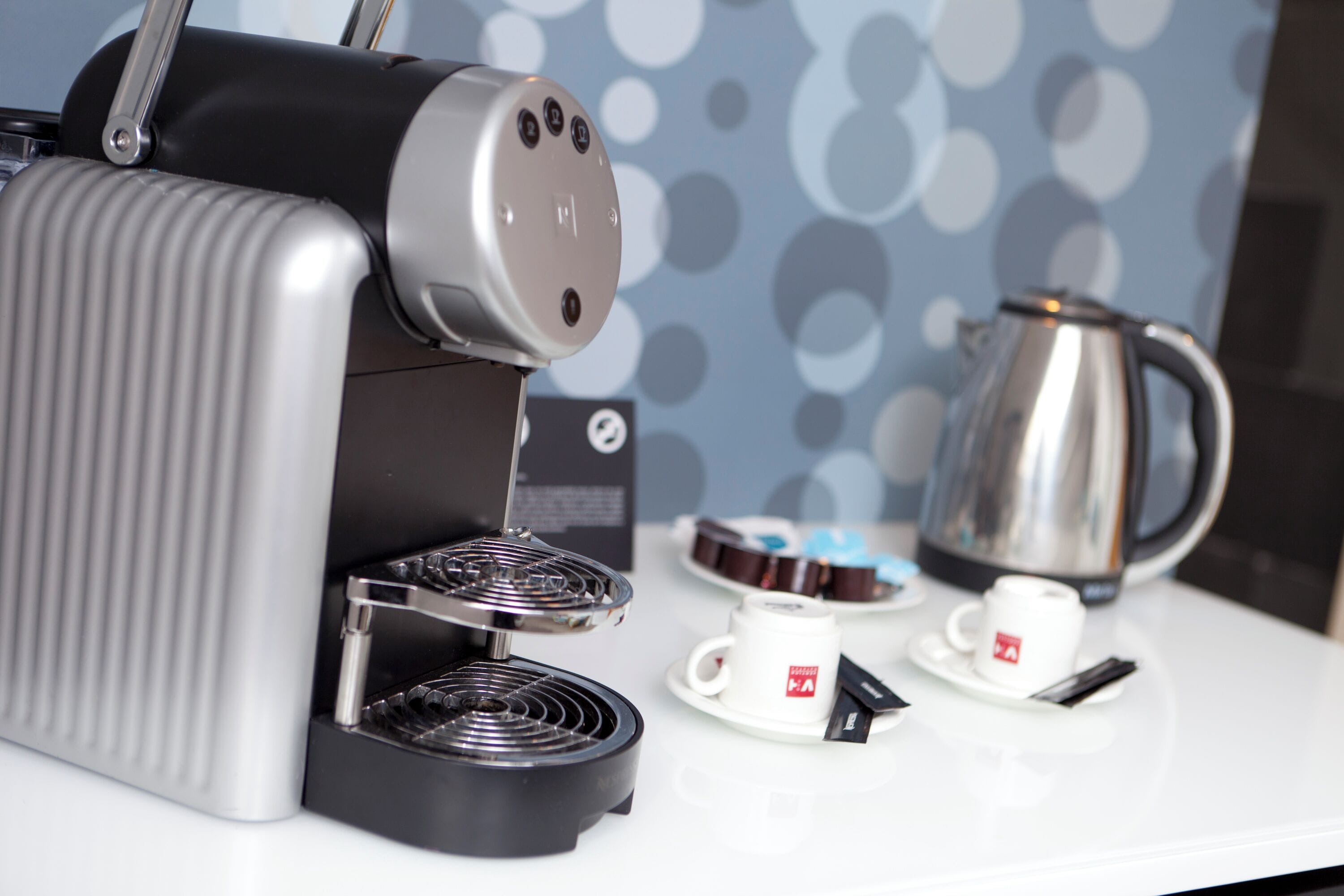 A coffee machine with a steam wand, a coffee pot, and two cups on a table.