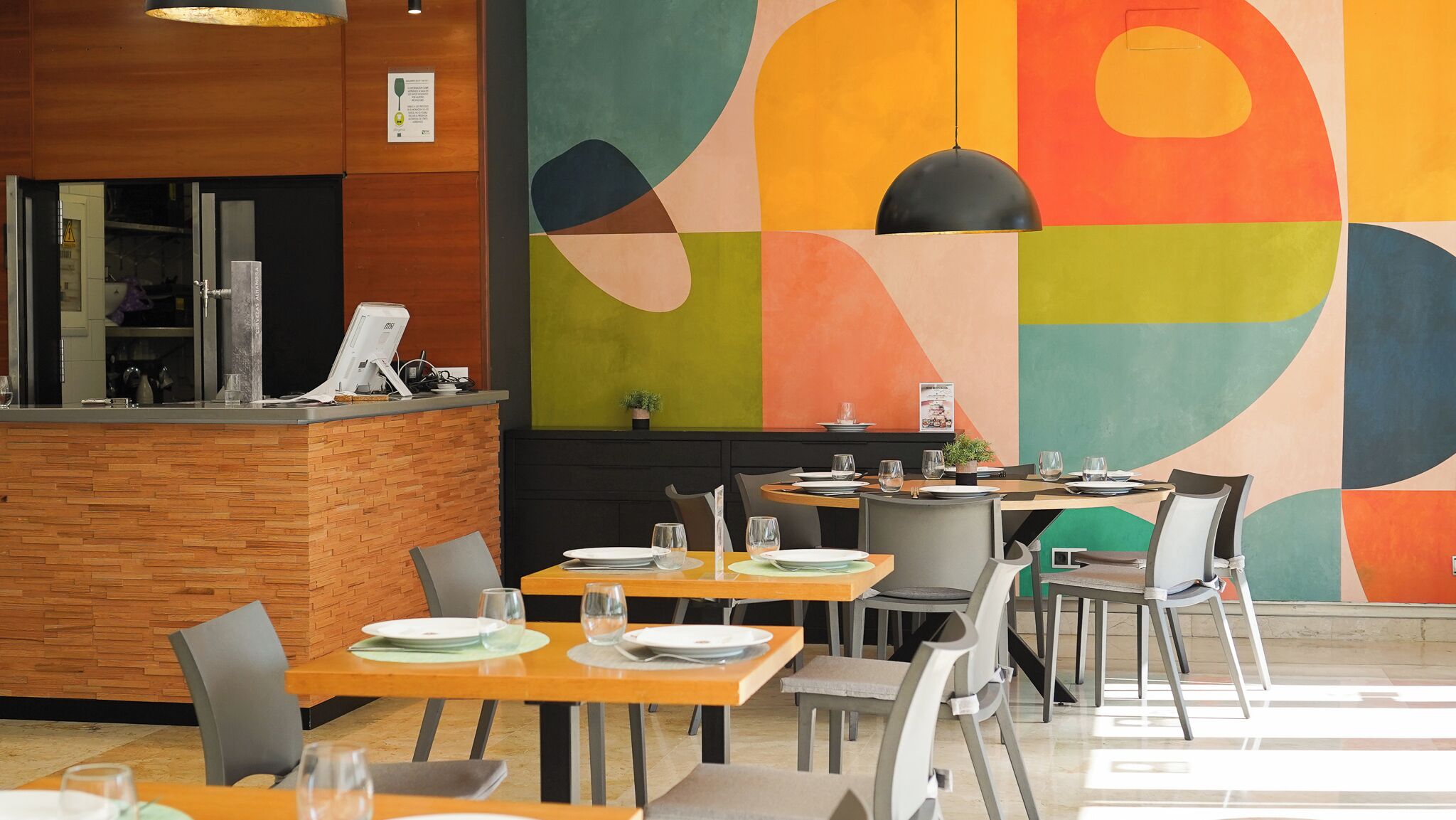 A modern restaurant interior with wooden accents, a colorful abstract wall, and a clean, organized dining area.