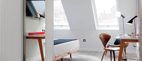 A modern bedroom with a bed, a desk, a chair, a mirror, and a window.
