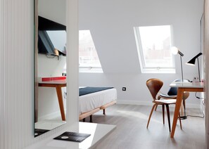 Een moderne slaapkamer met een bed, bureau, stoel, spiegel en raam.