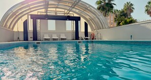 An indoor swimming pool with clear water, surrounded by white lounge chairs and a glass ceiling structure. - Hotel Vértice Sevilla (Seville)