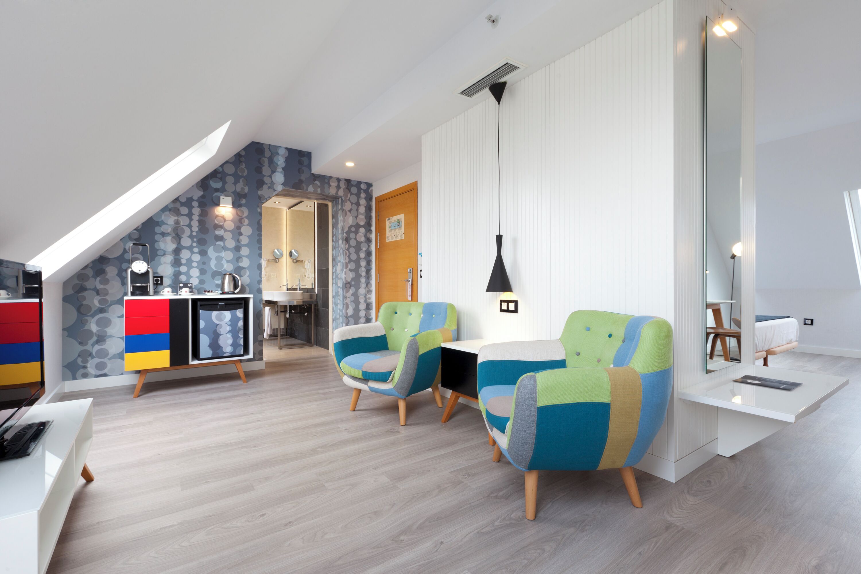 Un interior moderno con techo tipo loft, una kitchenette, sillones coloridos y un espejo grande.