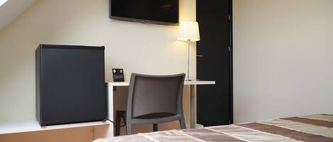 A small, modern hotel room with a bed, a desk with a chair, a flat-screen TV, and a lamp.