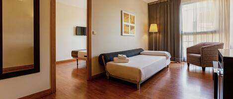 Habitación de hotel con cama, escritorio, silla, televisor y ventana con cortinas.