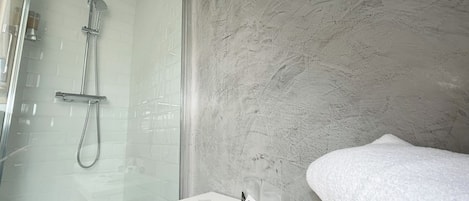 A modern bathroom with a glass shower enclosure, a marble wall, and a white vanity with toiletries.