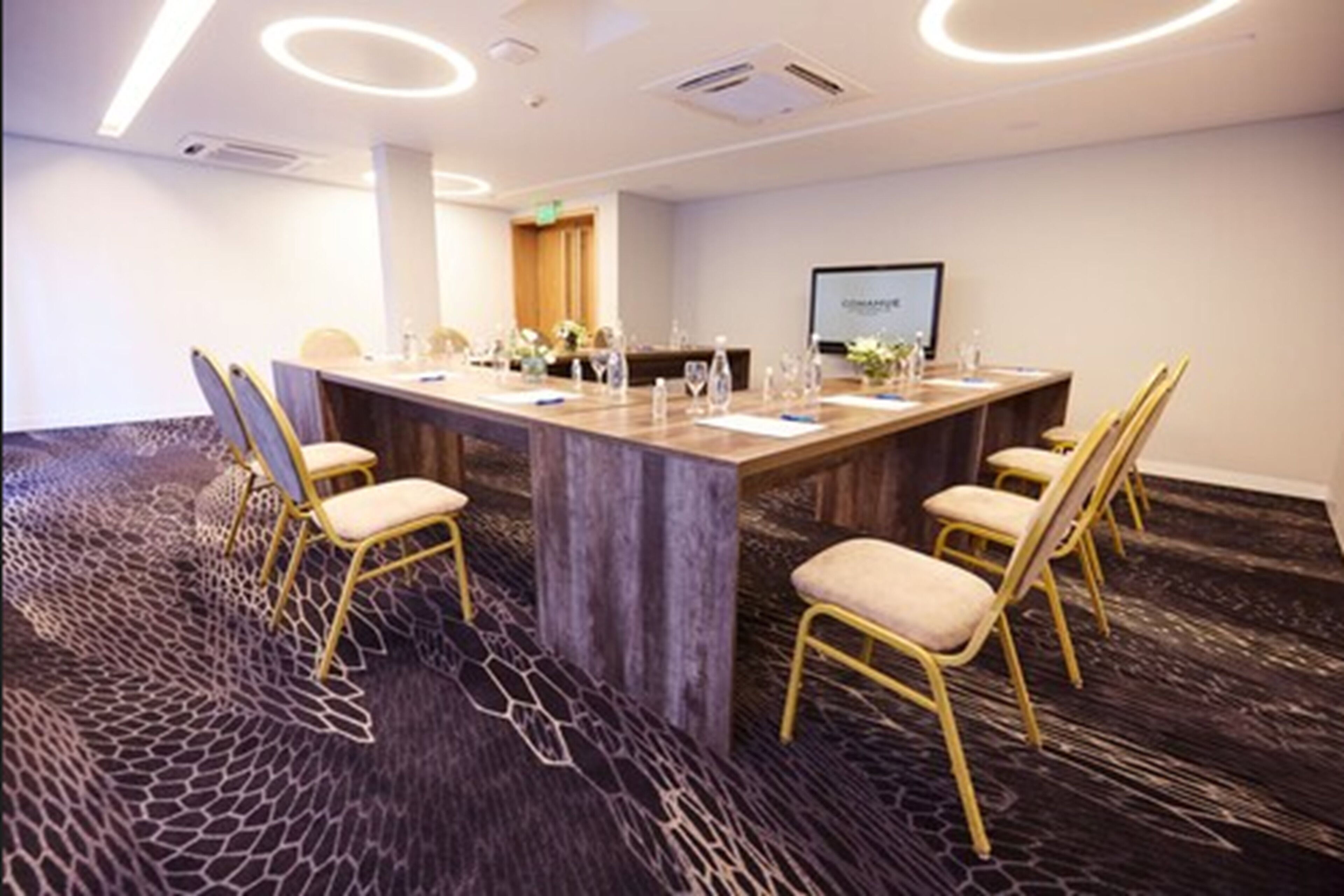 Een vergaderzaal met een lange tafel, stoelen en een scherm.