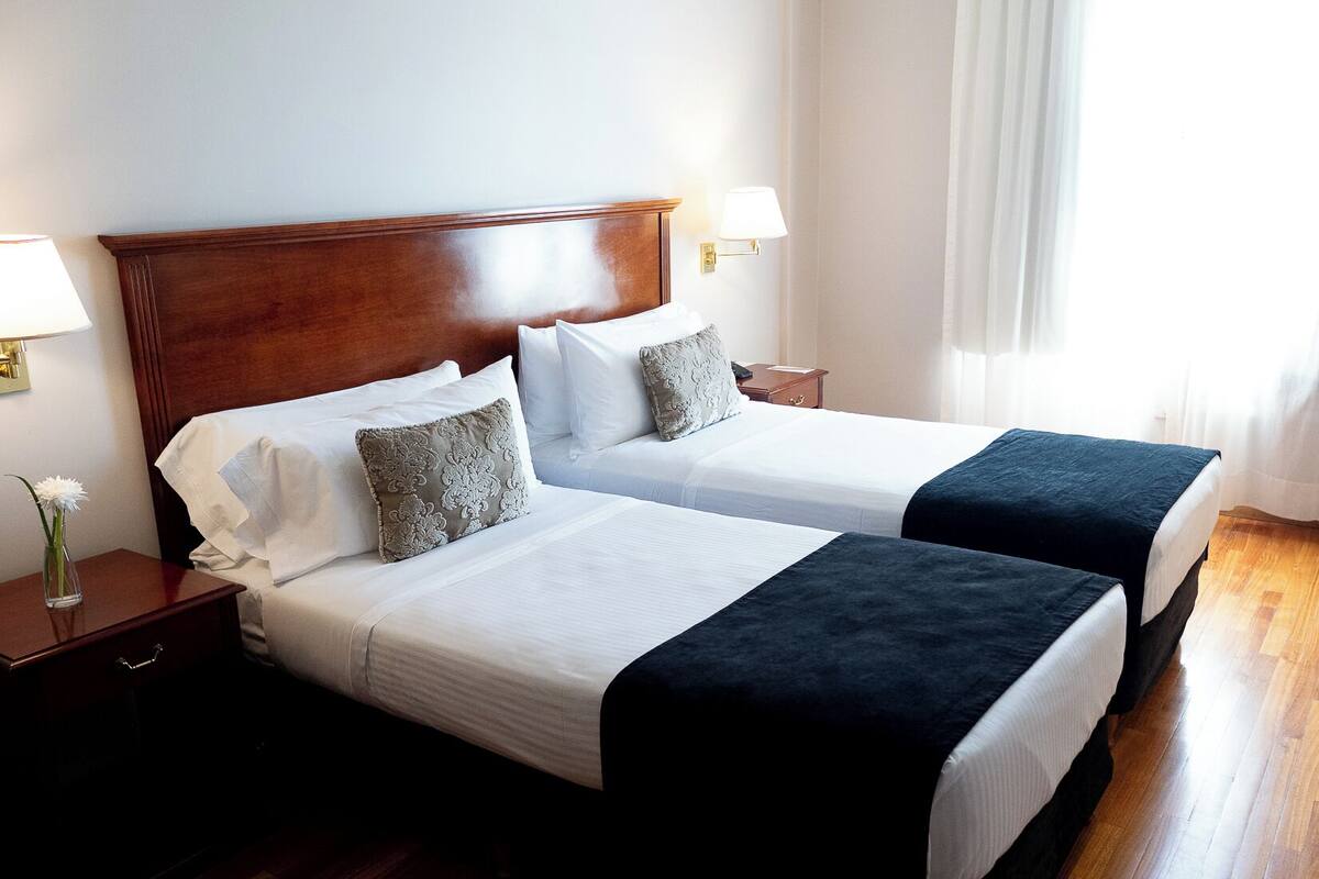 Ein Hotelzimmer mit zwei Betten, Holzboden und einem großen Fenster mit Vorhängen.