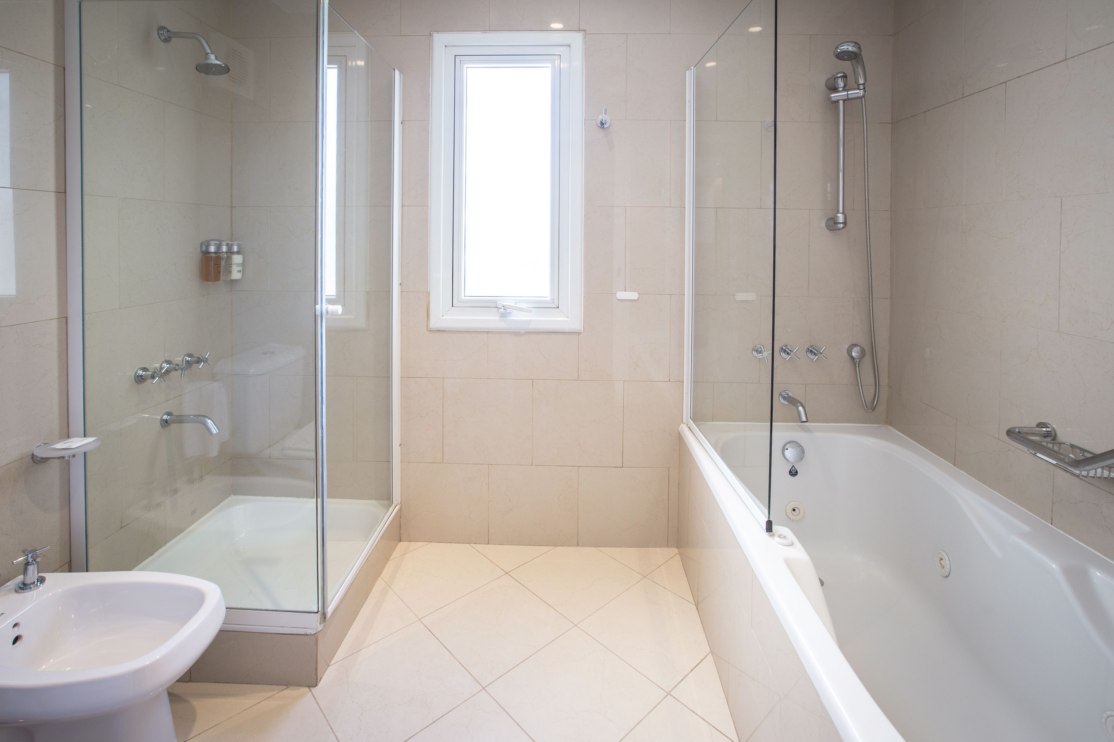Un baño moderno con ducha envuelta en vidrio, bañera independiente y lavamanos sobre pedestal.