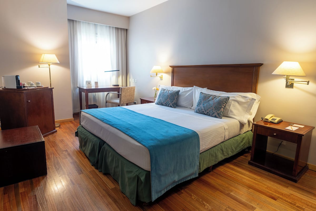 Ein Hotelzimmer mit einem großen Bett, Nachttischlampen, einem Schreibtisch mit Lampe und einem Sessel.