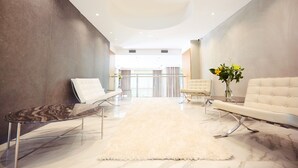 Un interior moderno con piso de mármol, alfombra blanca y mullida, un sofá, una silla y una mesa.