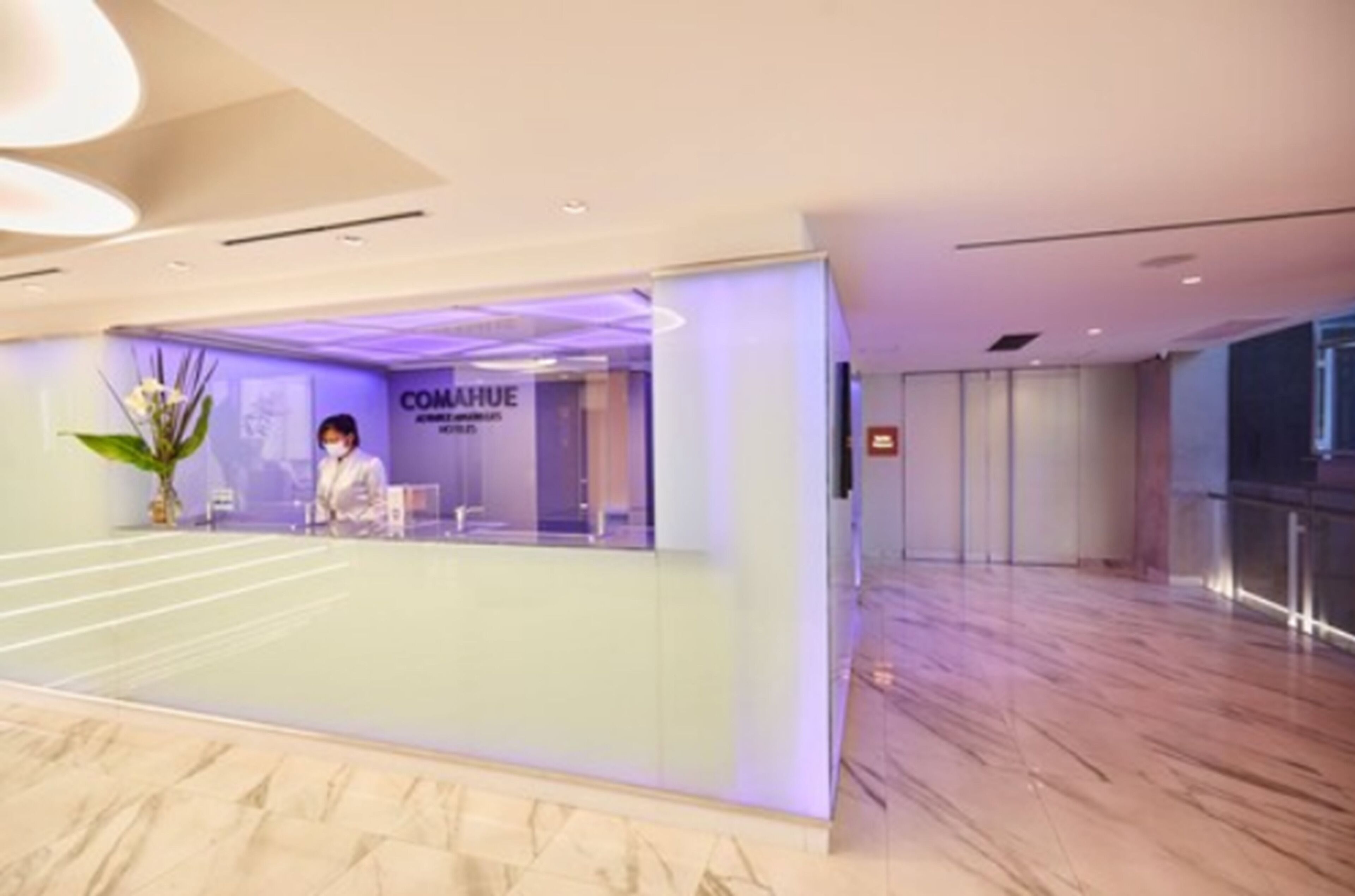 Un área de recepción de hotel moderna con un separador de vidrio, un mostrador de recepción y un letrero que dice "COMAHUE".