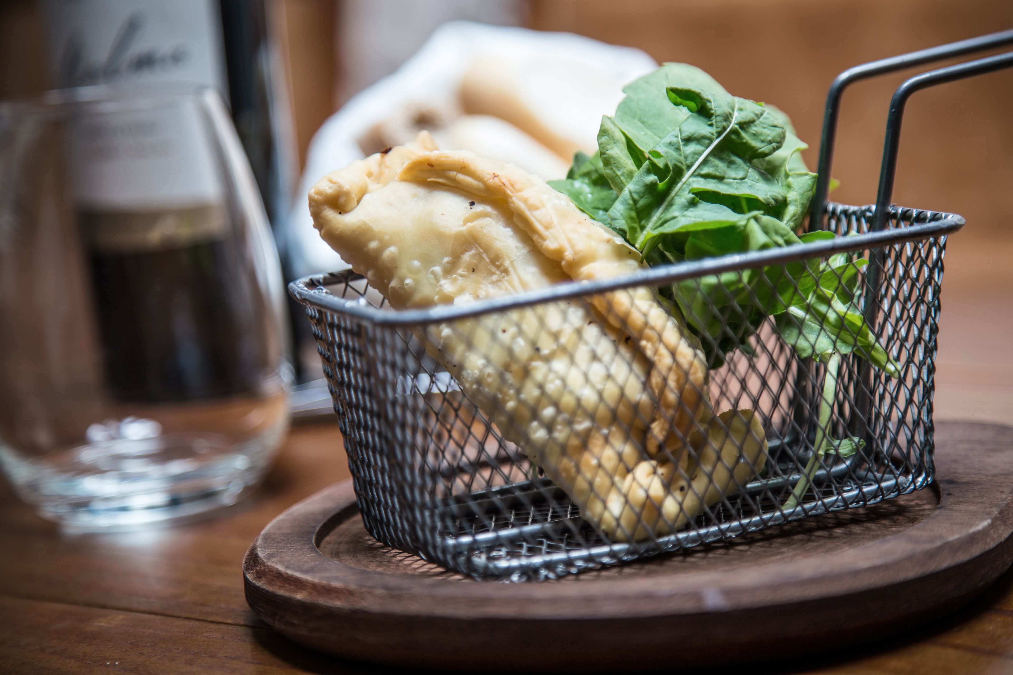 A basket containing a pastry and greens on a wooden coaster.