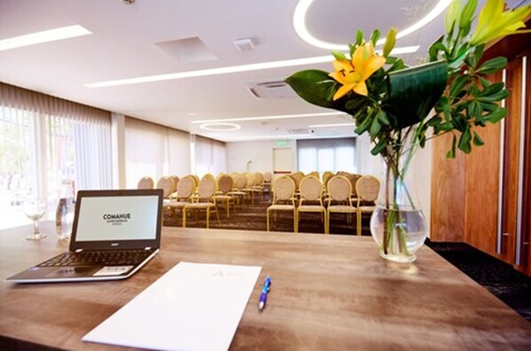 A conference room with a laptop displaying "COMANUE," a wooden table with a vase of flowers, and rows of chairs. - Gran Brizo Comahue (Neuquén)