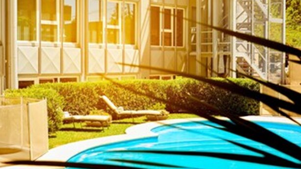 Un edificio moderno con una amplia fachada de vidrio, piscina y césped bien cuidado con sillas de descanso.