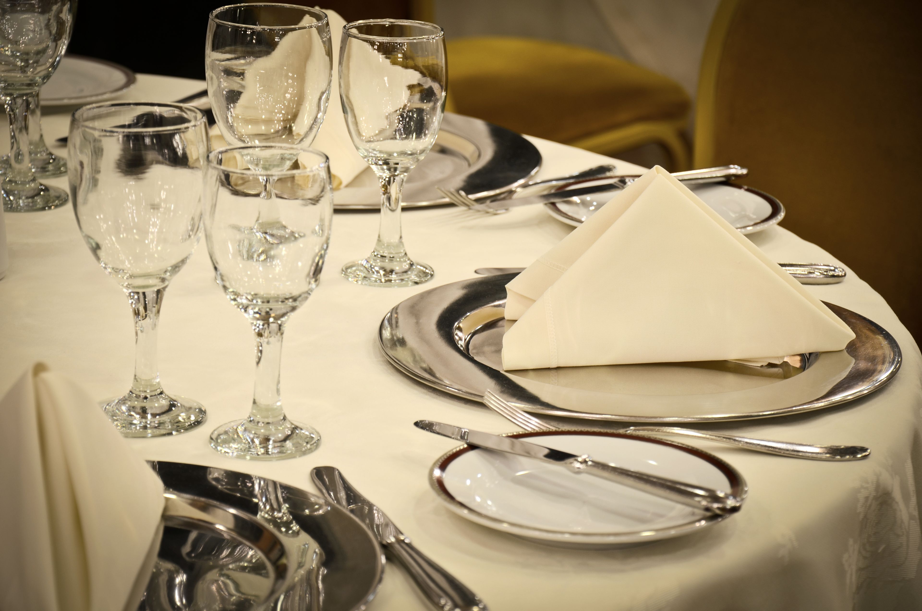 Mesa dispuesta con cubiertos, platos y copas de cristal, mostrando una disposición formal para el comedor.