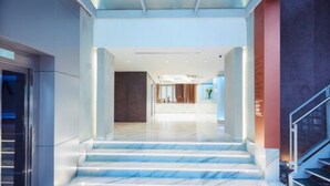 Un moderno vestíbulo de hotel con suelo de mármol, una escalera y techo de cristal.