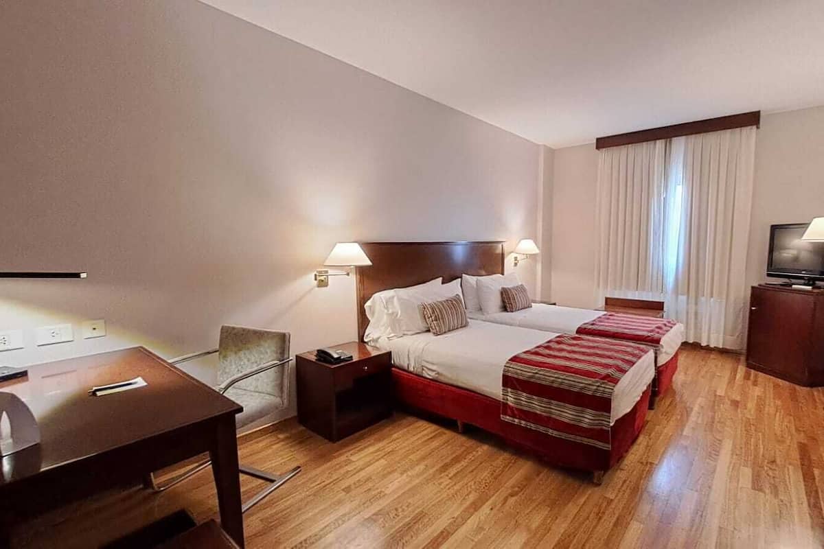 Ein Hotelzimmer mit Bett, Nachttischen, Schreibtisch und Fernseher.