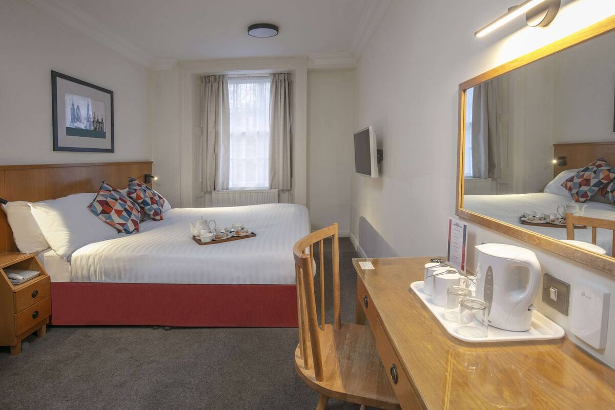 A hotel room with a bed, bedside table, chair, and a large mirror.