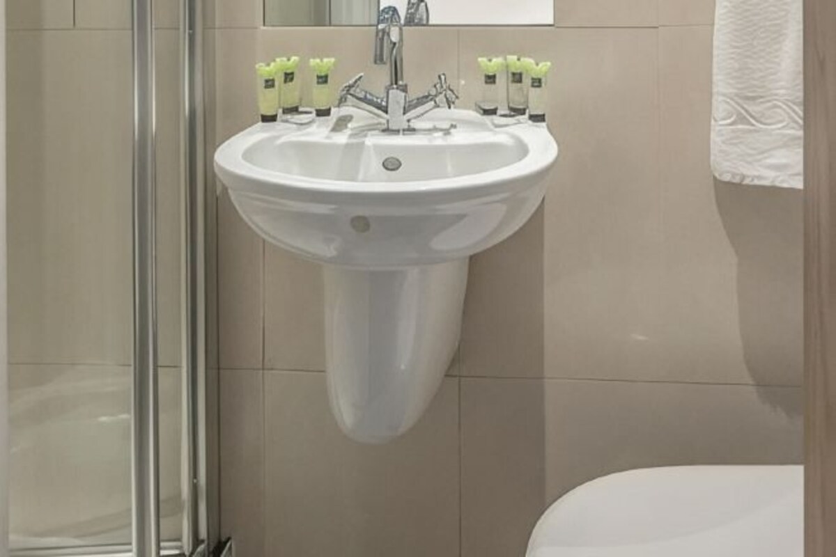 A bathroom with a white pedestal sink, a glass shower enclosure, and a white toilet.