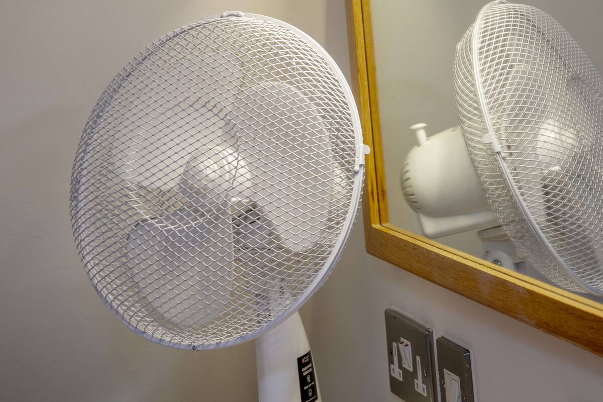 A white standing fan with a mesh cover, placed on a wooden surface.