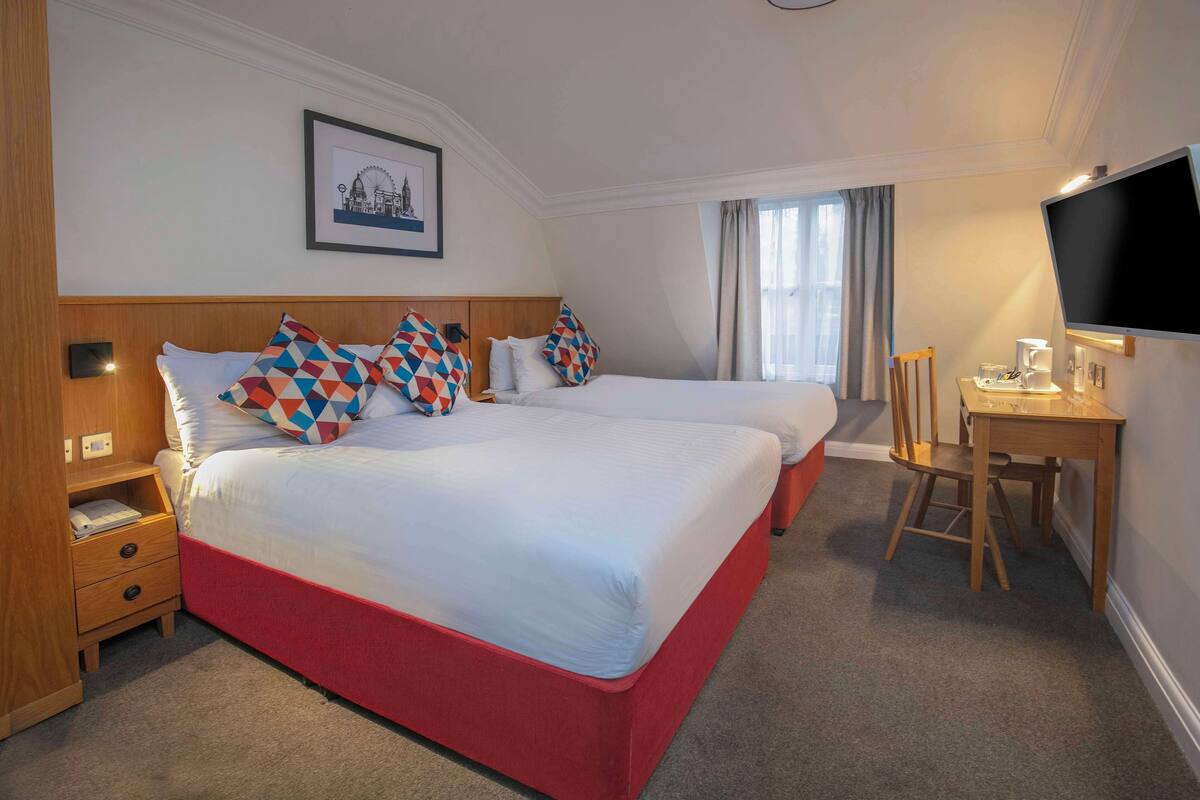 A hotel room with two beds, a desk, a chair, a TV, and a framed picture on the wall.
