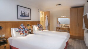 A hotel room with two beds, a wooden wardrobe, a desk with a chair, and a framed picture on the wall. - Queensway Hotel, Sure Hotel Collection by Best Western (London)