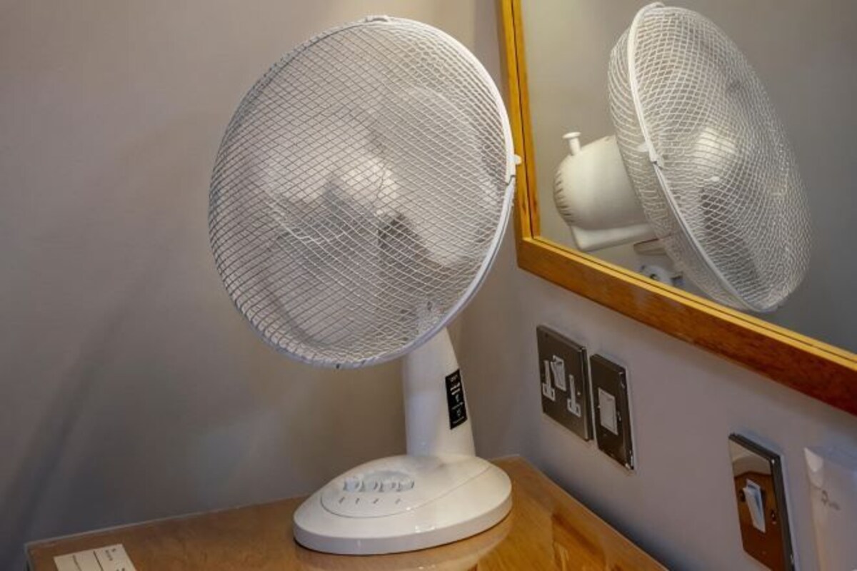 A standing fan with a mesh cover, a wooden table, and a wall-mounted mirror.