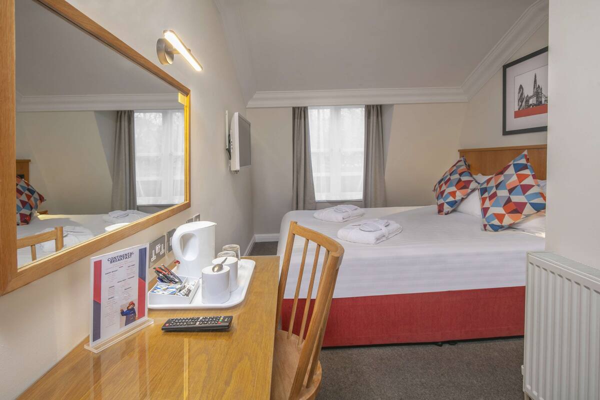 A hotel room with a bed, a desk with a remote control, a coffee maker, and a breakfast menu sign.