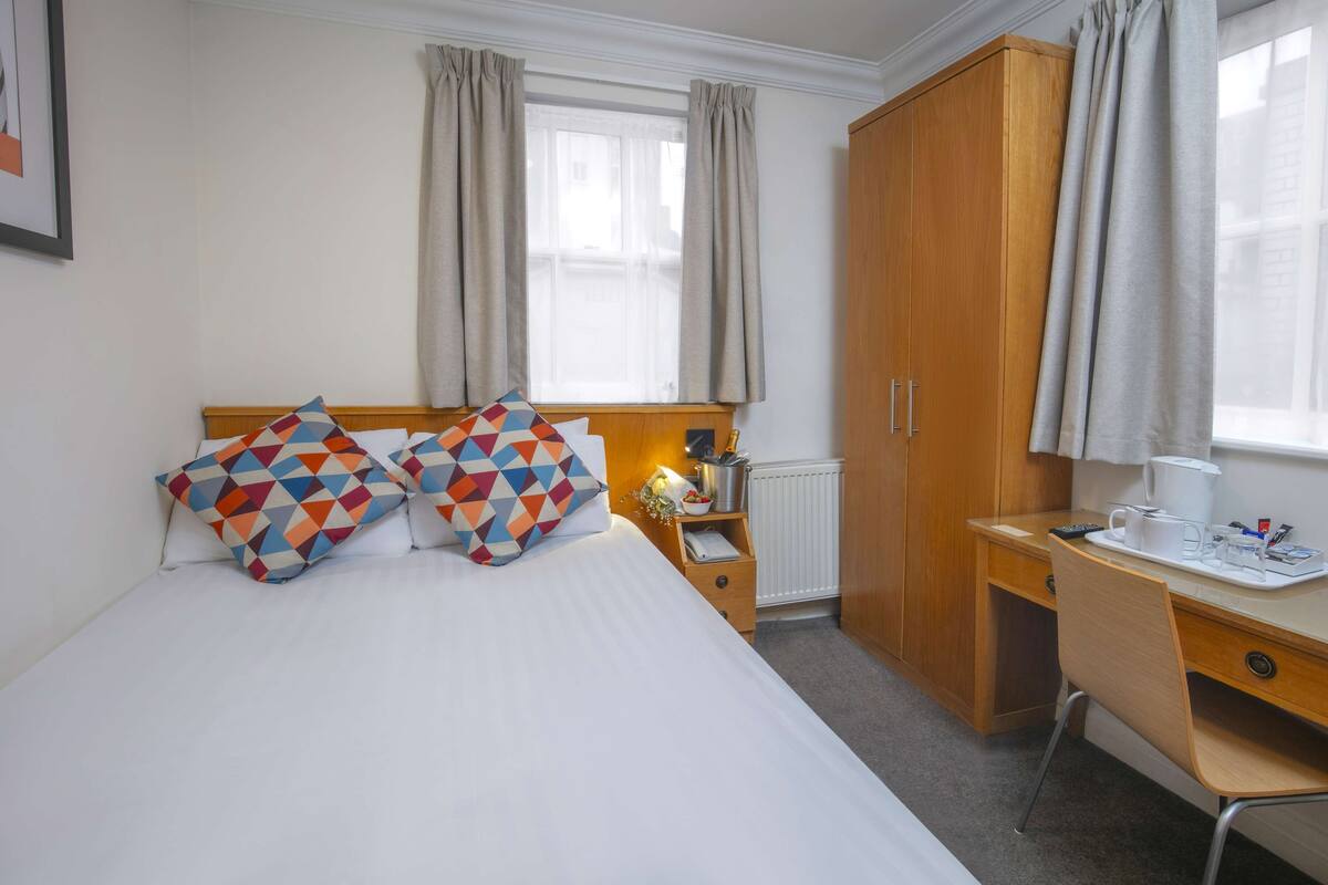 A neatly arranged bedroom with a bed, a desk, and a wardrobe.