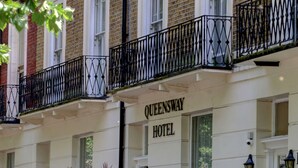 A building with a sign reading "Queensway Hotel." It features a white facade, black iron railings, and a gated entrance. - Queensway Hotel, Sure Hotel Collection by Best Western (London)