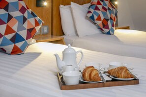 A neatly made breakfast tray with croissants, cups, and a teapot on a bed with a wooden headboard and patterned pillows. - Queensway Hotel, Sure Hotel Collection by Best Western (London)