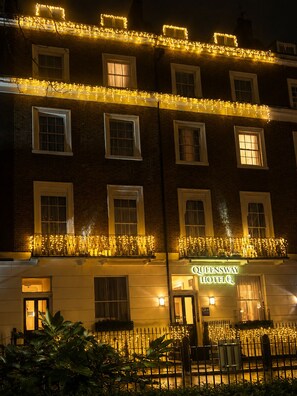 A hotel with multiple windows, a balcony with lights, and a sign indicating it's the Queensway Hotel. - Queensway Hotel, Sure Hotel Collection by Best Western (London)