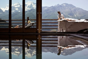 A spa room with a large window offering a mountain view, a massage table, and a reflection on the floor. - Chalet d'Adrien (Bagnes)