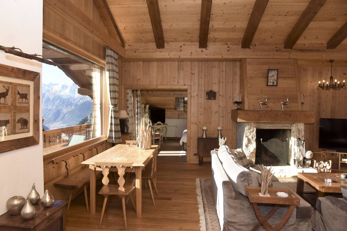 A wooden interior with a dining area, sofa, fireplace, and mountain view.