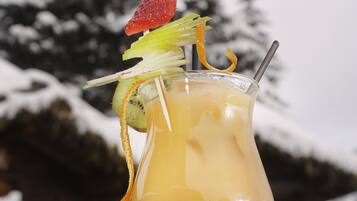 Un cocktail servi dans un verre, agrémenté d’une fraise et de tranches de kiwi, avec une paille, posé sur une table devant un décor enneigé.