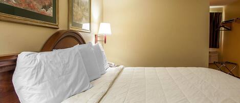 A hotel room with a large bed, a wooden headboard, a painting on the wall, and a nightstand with a lamp.