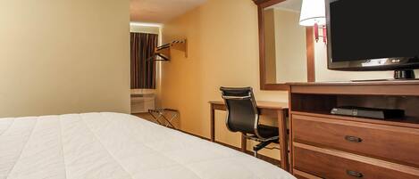 A hotel room with a bed, a desk with a chair, a television, and a mirror.